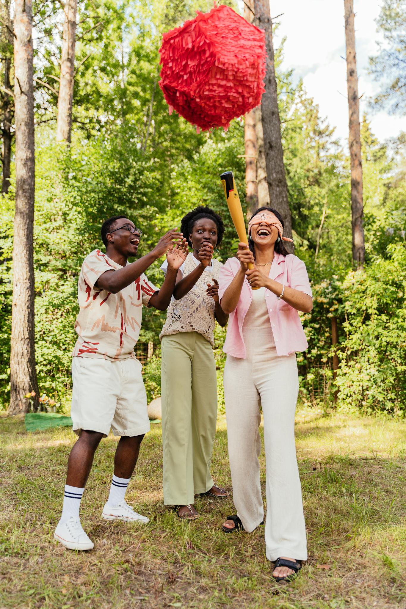 Group of friends playing with a pinata in a sunny forest setting, having fun together.